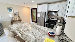 Una cocina moderna con armarios blancos, electrodomésticos de acero inoxidable, encimera de mármol y comedor con banco y sillas.