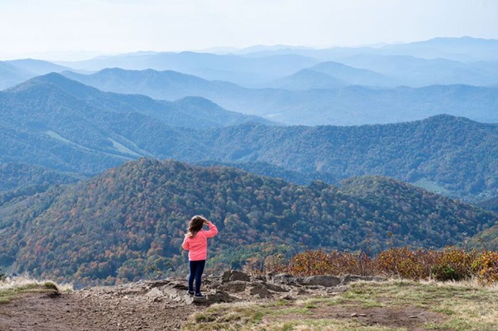 A person standing on a rocky outcrop overlooking a mountainous landscape.