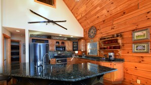 Una cocina con encimeras de granito, gabinetes de madera, un refrigerador de acero inoxidable y un reloj en la pared.