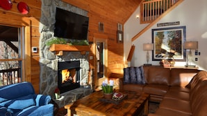 Una sala de estar acogedora con chimenea de piedra, un sofá azul, un sofá de cuero marrón y una mesa de centro de madera.