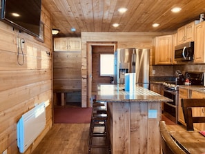 Ein Holzblockhaus-Interieur mit einer Küche, die eine zentrale Kochinsel, Barhocker, Holdeinrichtungen und eingebaute Geräte umfasst.