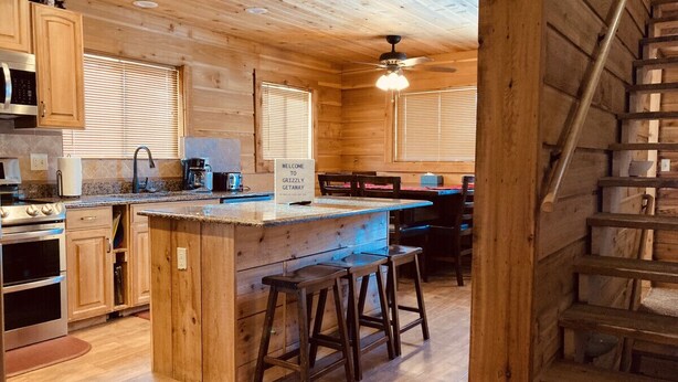 A wooden cabin interior with a kitchen area featuring a bar, wooden cabinets, a stove, and a ceiling fan. - 12 miles to Yellowstone National Park, hot tub, fire pit, 3 bedrooms 3 bathrooms (Island Park)
