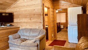 A cozy cabin interior with a plush sofa, a wooden wall, a television, and a refrigerator. - 12 miles to Yellowstone National Park, hot tub, fire pit, 3 bedrooms 3 bathrooms (Island Park)