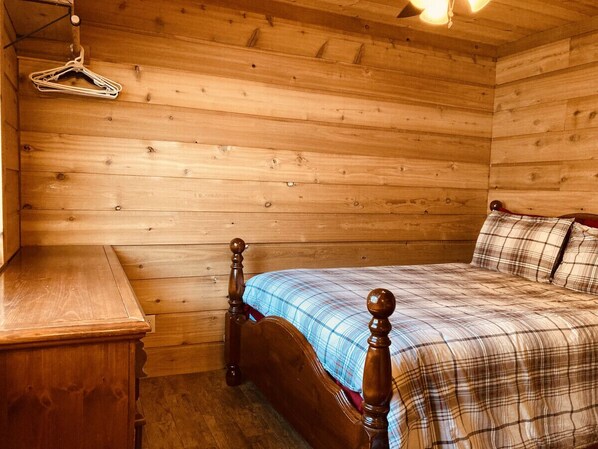 A wooden room with a bed, a wooden dresser, and a hanging clothes rack.