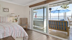 Ein Schlafzimmer mit Bett, Stuhl, Schreibtisch, Lampe und Meerblick durch eine Schiebetür.