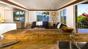 A modern kitchen with a large island, a dining area with a black sofa, and a view of the ocean through large windows.