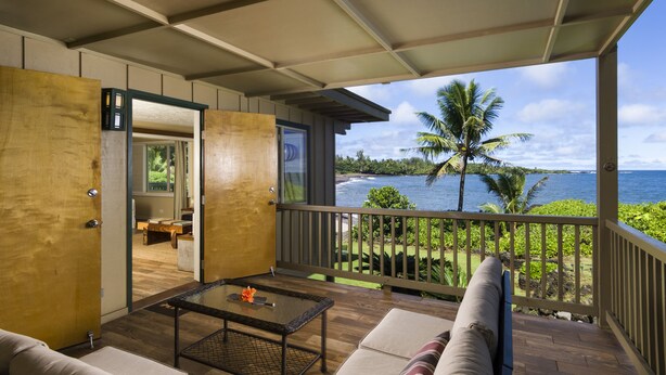 A room with a wooden floor, a glass coffee table, a sofa, and a view of the ocean.