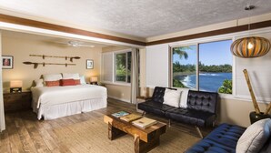 A bedroom with a bed, a sofa, a coffee table, and a view of a body of water through large windows.