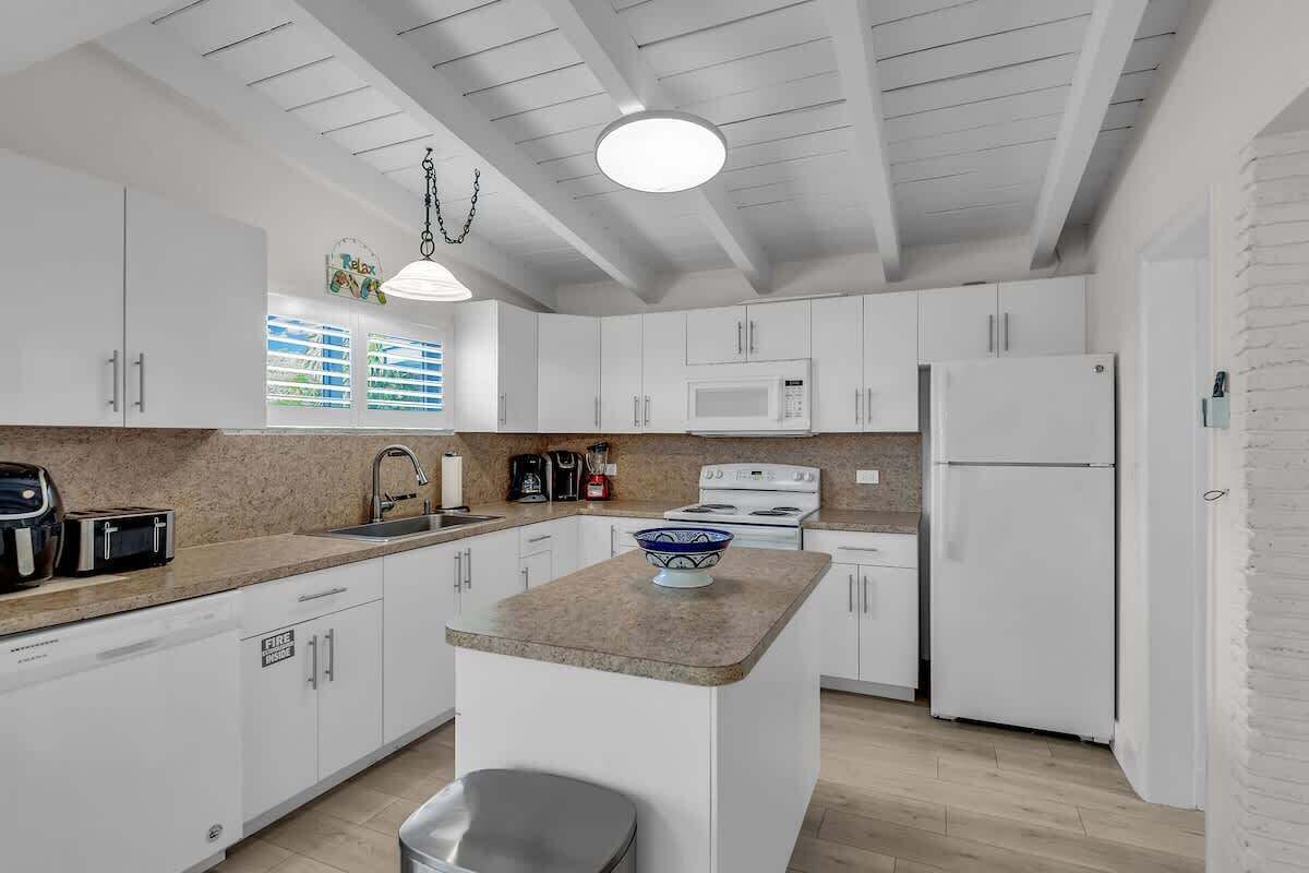 Una cocina moderna con armarios blancos, una isla central, un microondas, una estufa y un refrigerador.