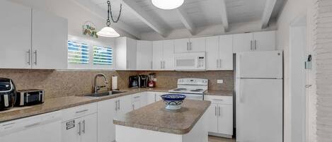Una cocina moderna con armarios blancos, una isla central, un microondas, una estufa y un refrigerador.