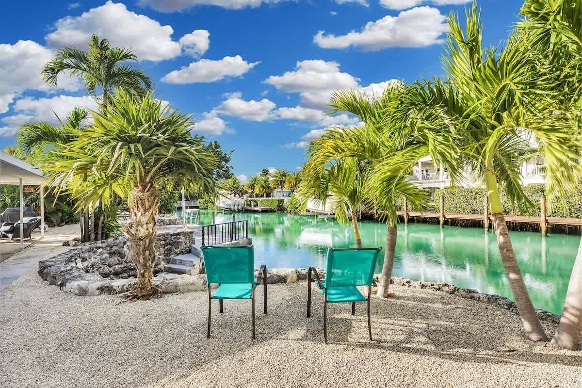 Een zwembadgedeelte met palmbomen, een heldere lucht en twee groene stoelen.
