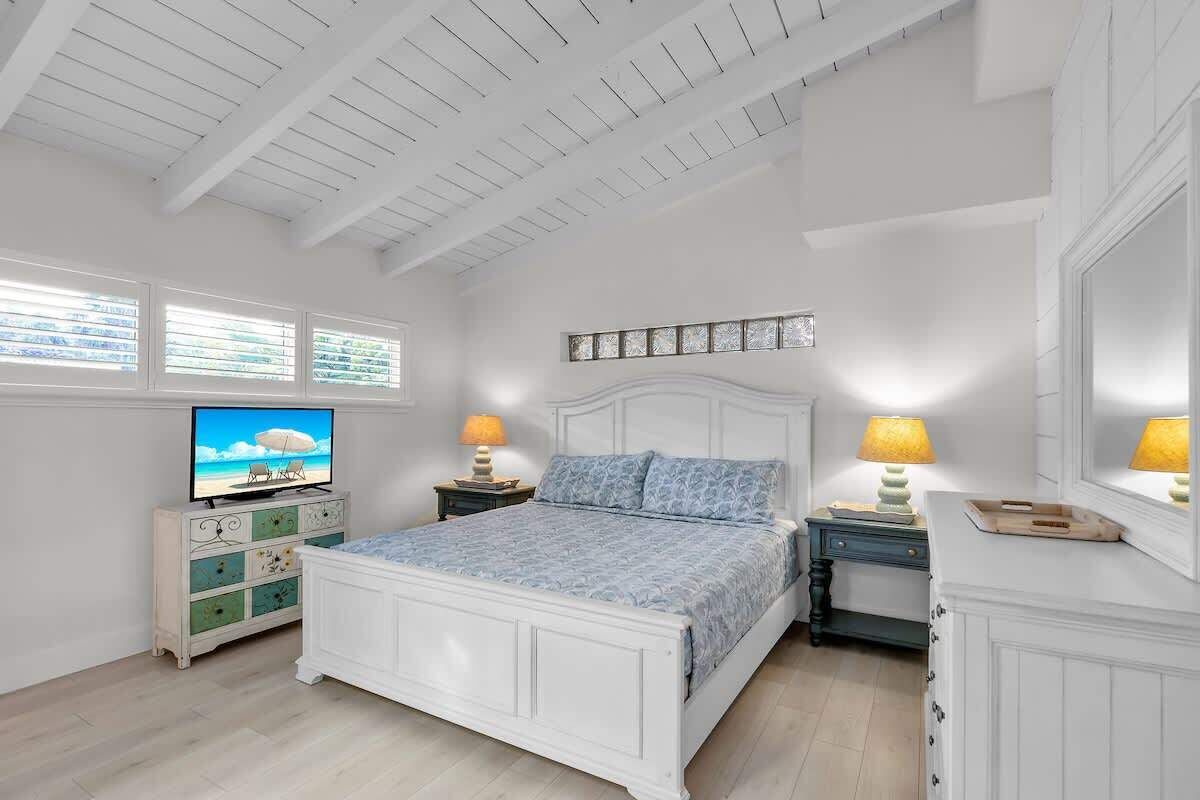 A bedroom with a bed, a dresser, a TV, and two bedside tables with lamps.