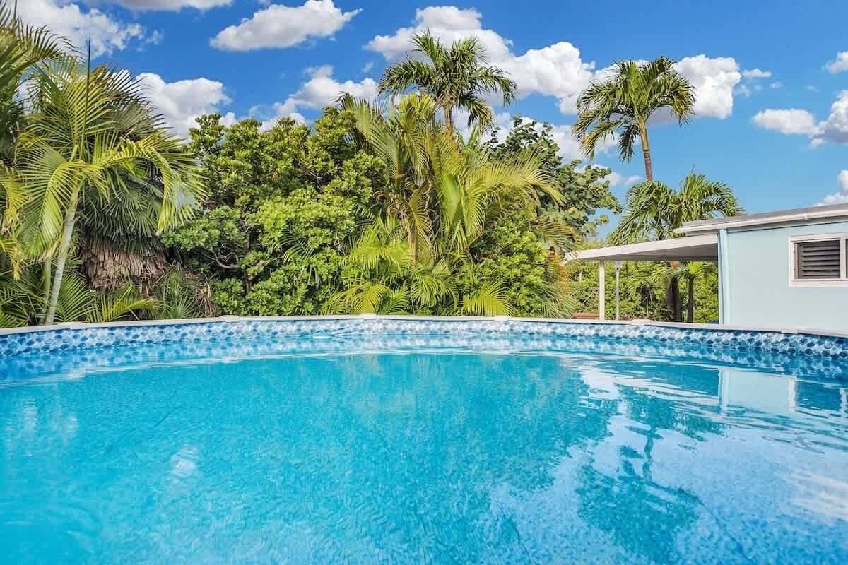 Piscina azul cristalina rodeada de vegetación exuberante y un edificio azul claro.