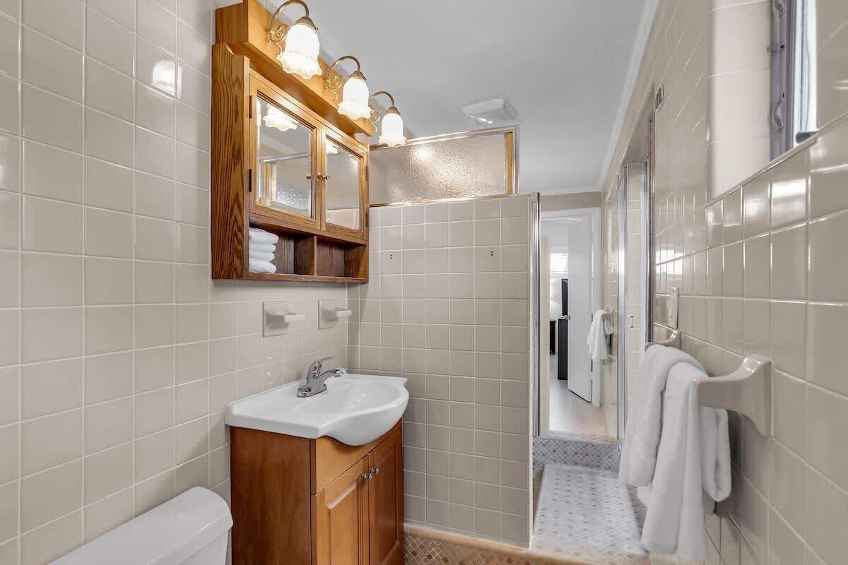 A bathroom with a wooden vanity, a white sink, a mirror with lights, and a shower area.