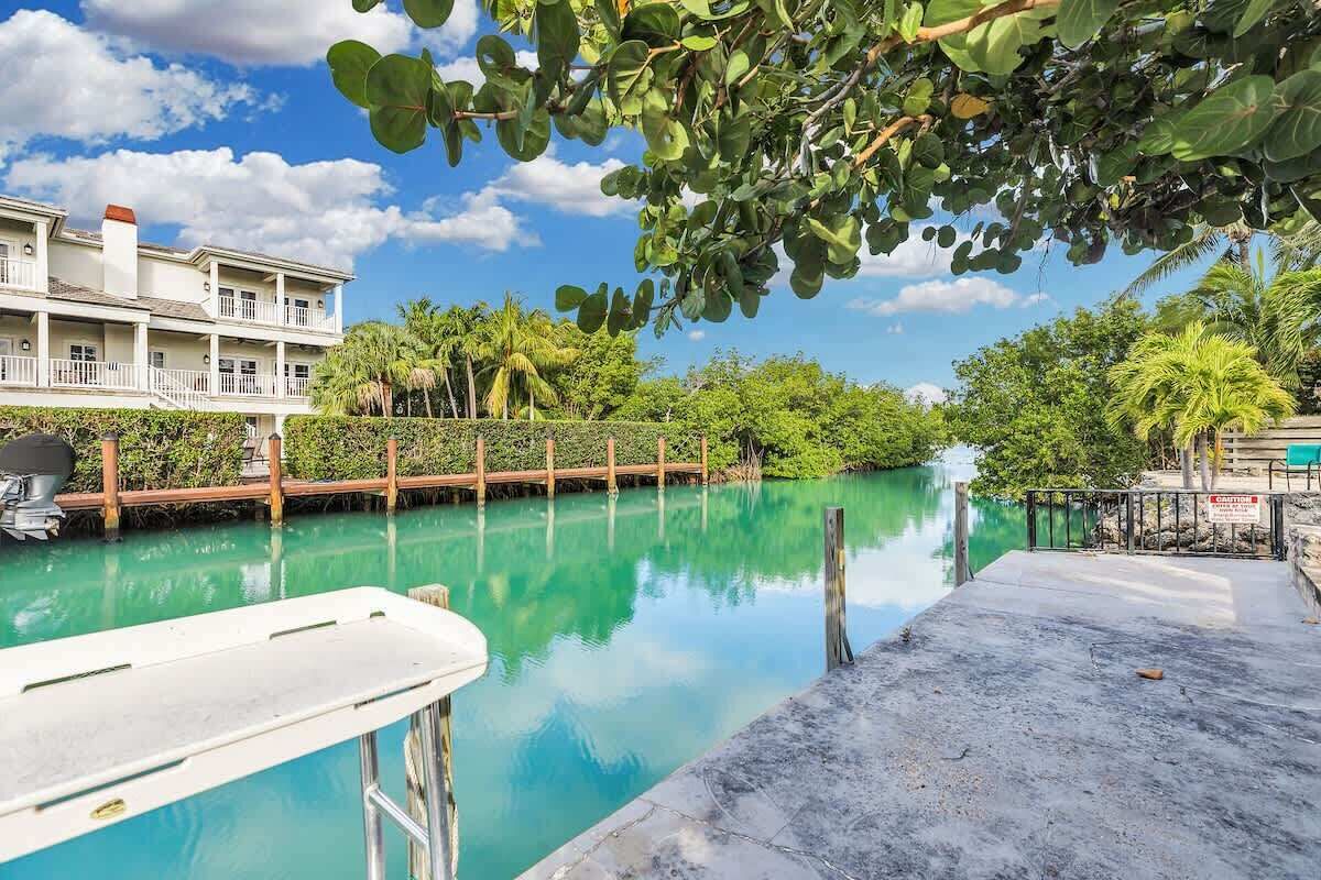 A swimming pool with a wooden deck, surrounded by lush greenery and a building with balconies.