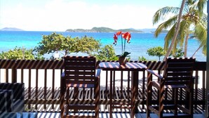 A wooden deck with two chairs and a table, overlooking a turquoise sea with distant hills. - IMMACULATE! WASTE NO TIME GETTING TO THE BEACH! (St. Thomas)