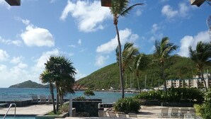 A pool area with lounge chairs, a stone wall, and a view of the sea and a hill in the background. - IMMACULATE! WASTE NO TIME GETTING TO THE BEACH! (St. Thomas)