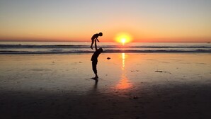 Une scène de plage au coucher du soleil, où l’on voit une personne et un enfant jouant dans le sable.