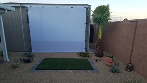 A backyard with a white screen, a green lawn, and various plants.