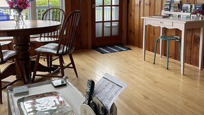 Una habitación acogedora con paredes de madera, una mesa de comedor con sillas, un escritorio pequeño con una silla y una ventana con vistas al exterior.