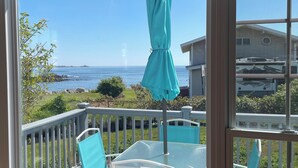 Una terraza con sillas y una mesa, con vistas a un cuerpo de agua y una costa distante.