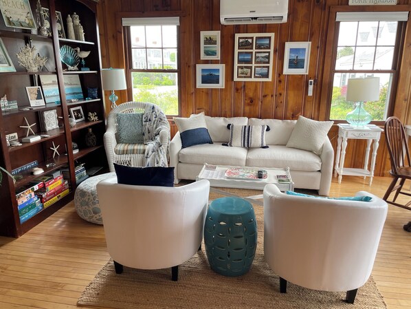 A cozy living room with a white sofa, two armchairs, a coffee table, and a bookshelf filled with books and decorative items. - Beautiful ocean views & walking distance to the beach. (York)