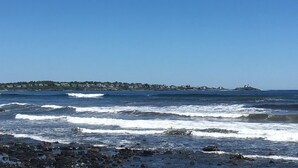 Vista costera con olas, una costa rocosa y un pueblo lejano con edificios.