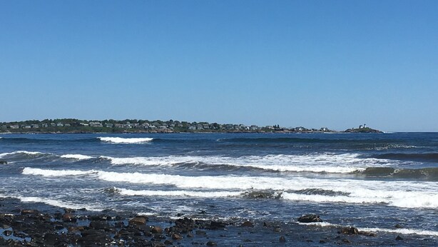 Une vue sur la côte, avec des vagues, une côte rocheuse et une ville lointaine avec des bâtiments.