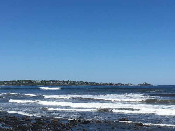 A coastal view with waves, a rocky shoreline, and a distant town with buildings. - Beautiful ocean views & walking distance to the beach. (York)