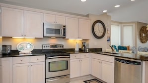 Una cocina moderna con electrodomésticos de acero inoxidable, armarios de colores claros y un reloj de pared grande.