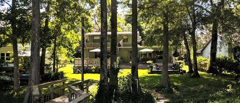 A cabin with a deck, surrounded by trees and a small pond.