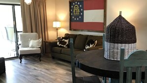 Een woonkamer met een eettafel, een plafondventilator, een vlag aan de muur en een lamp.