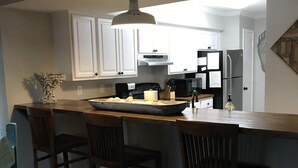 Een keuken met een centraal eiland, barstoelen, een hanglamp en witte kastjes.