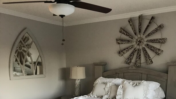 Een slaapkamer met een houten bed, een plafondventilator, een decoratief object aan de muur en een spiegel.