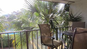 A balcony with a chair and table, overlooking a garden with palm trees and a view of buildings.