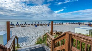 Une plage avec des passerelles en bois menant au sable, une rangée de parasols et une vue dégagée sur l’océan.