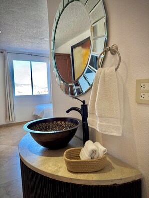 A bathroom with a round mirror, a sink with a bowl, a towel, and a window with curtains.