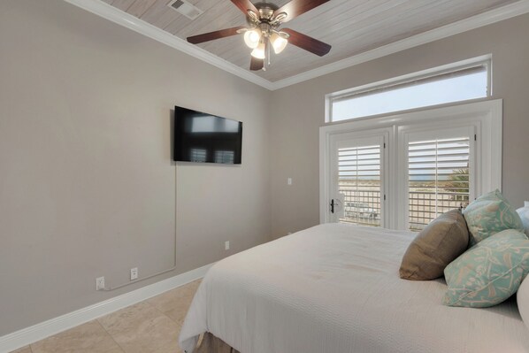 A bedroom with a ceiling fan, a TV mounted on the wall, a bed with pillows, and a window with blinds. - 🌴 Beach Getaway 🌴 Steps to Beach w/ Pool + Sleeps 22 + Gulf Views (Pensacola Beach)