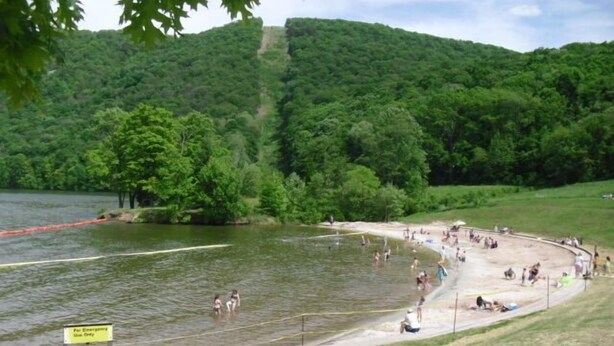 A lakeside park with a swimming area, a picnic area, and a trail leading up a hill.