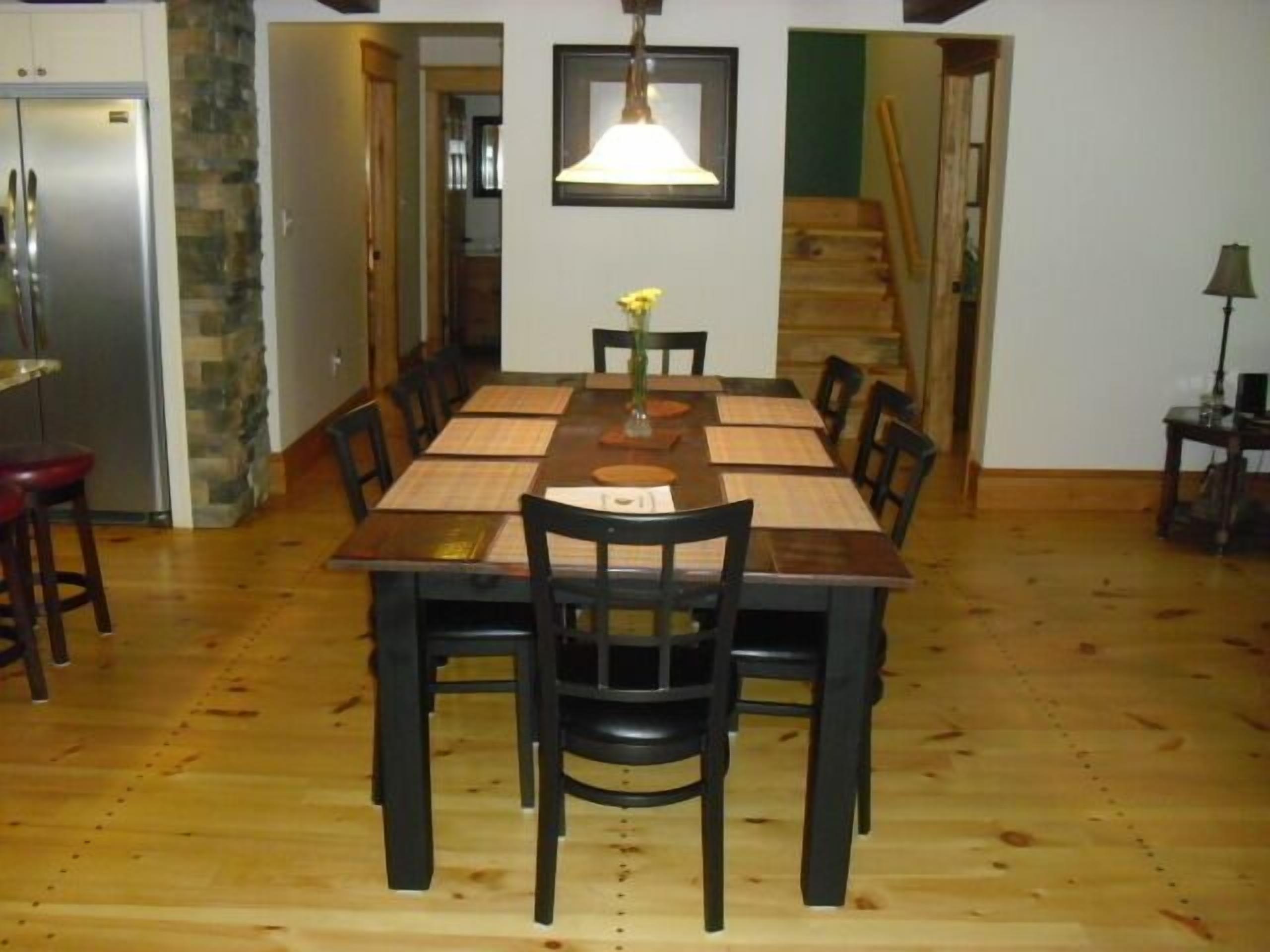 Een eetkamer met een lange houten tafel, zwarte stoelen, een hangende lamp en een stenen muur.