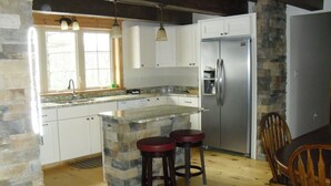 A kitchen with a stone island, wooden stools, and a stainless steel refrigerator.