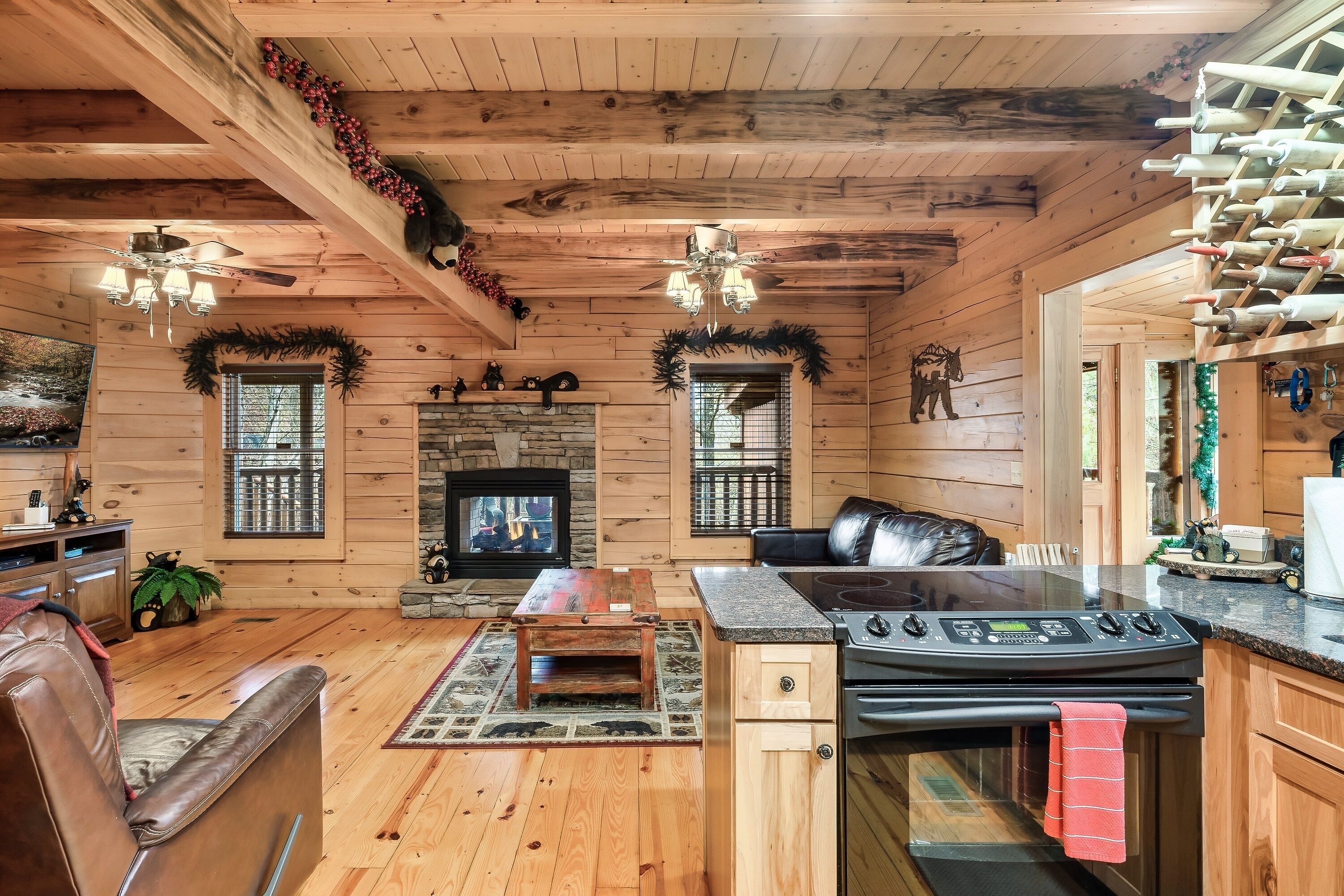 Interior acogedor de una cabaña con chimenea, paredes de madera, comedor y cocina con estufa y botellero.