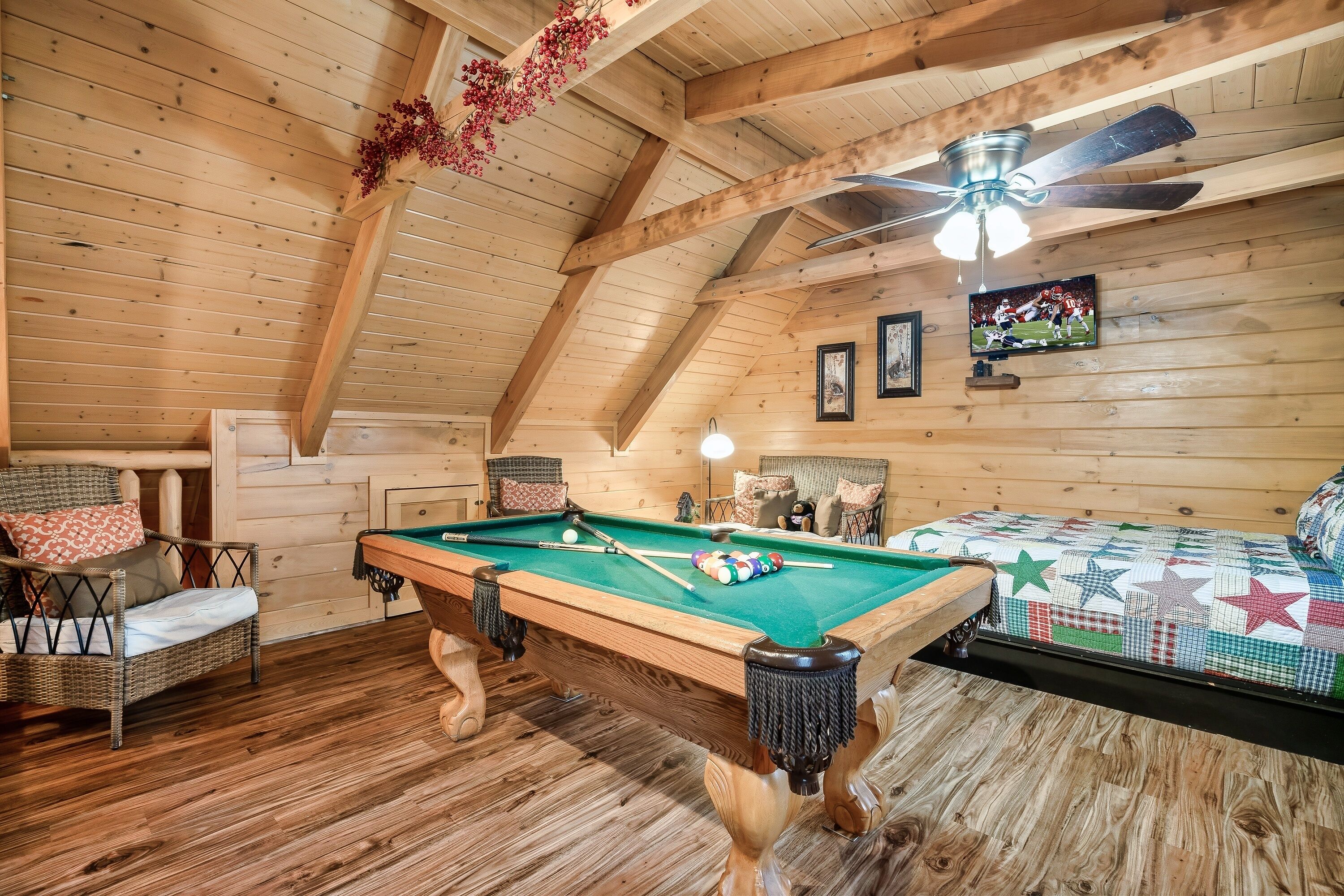 A cozy room with a pool table, wooden ceiling beams, a ceiling fan, and a television on the wall.