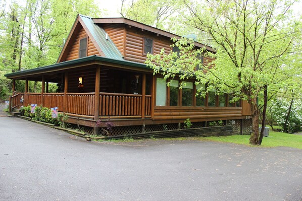 A wooden cabin with a porch, a covered deck, and a large window overlooking the surrounding forest. - Hidden Treasure in the heart of Pigeon Forge
50.00 off a night jan. and feb. (Pigeon Forge)