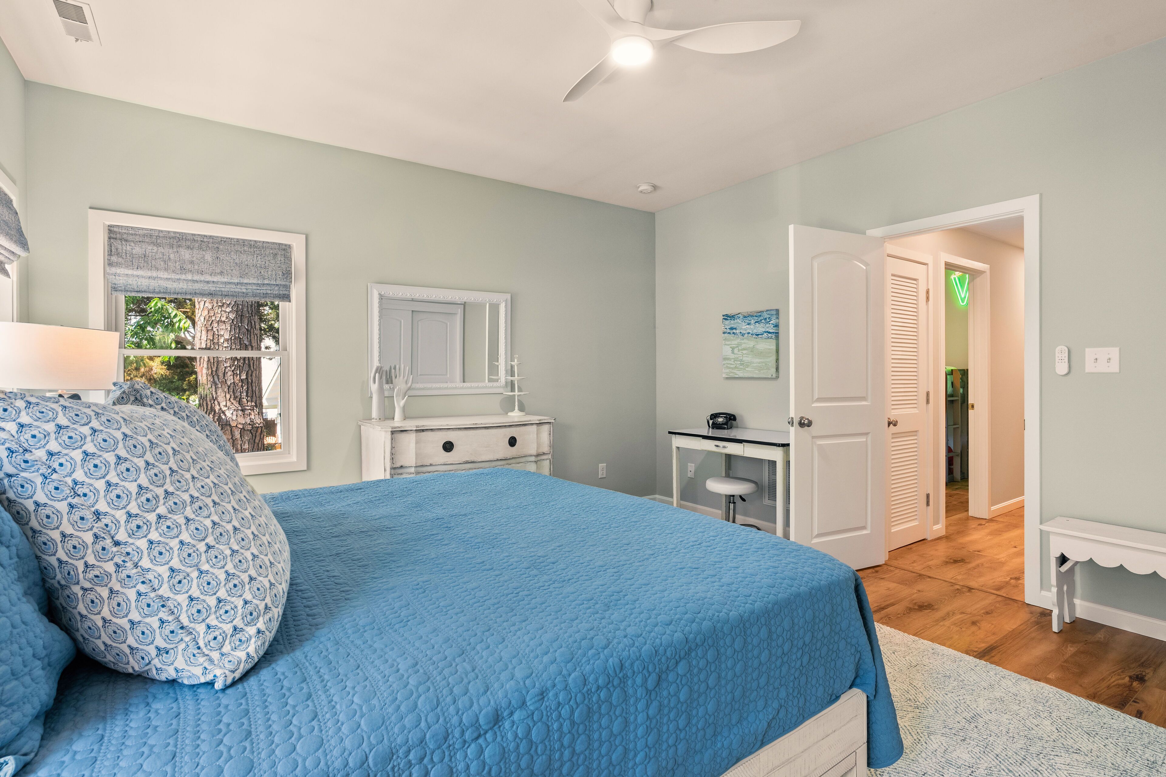 Un dormitorio con cama, cómoda, escritorio y puerta que da a otra habitación.