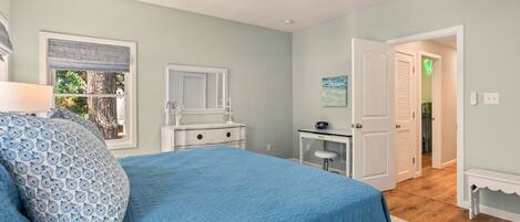 Un dormitorio con cama, cómoda, escritorio y puerta que da a otra habitación.