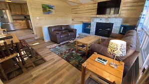 Interior acogedor de una cabaña con sala de estar, chimenea, muebles de madera y zona de cocina.