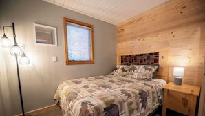 Un dormitorio con cama, una mesita de noche con lámpara, una lámpara de pie, una ventana con persianas y un cabecero de madera.