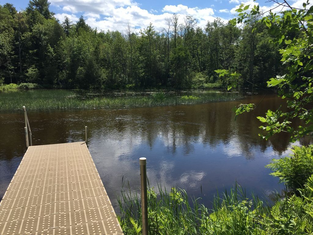 Une jetée en bois s’étendant sur un lac paisible, entouré d’une forêt dense.