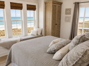 Un dormitorio con vista a la playa, un armario de madera y un banco junto a la ventana.